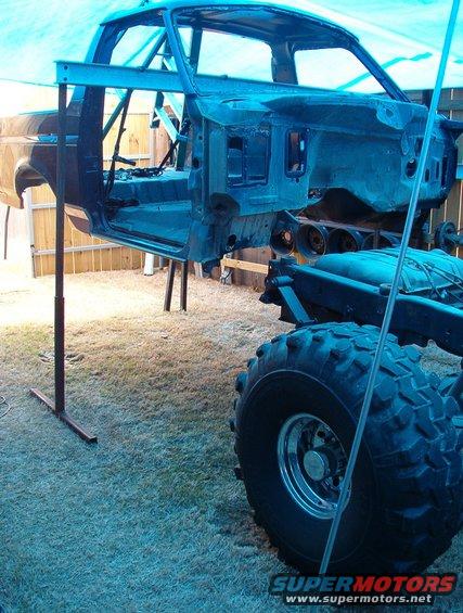 Blue Ford Bronco body lifted on a stand, showing the chassis and large off-road tire