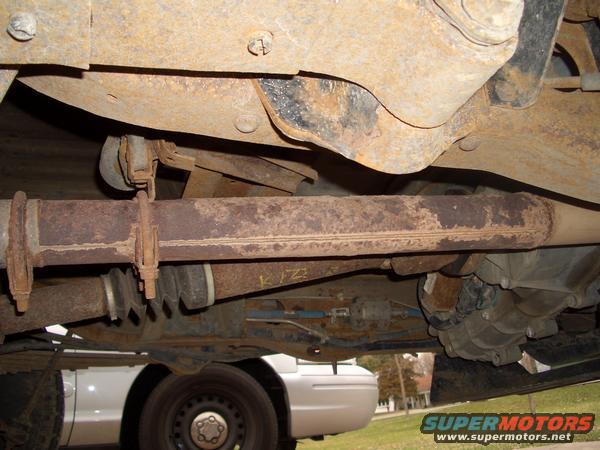 Undercarriage of a rusty vehicle, showing exhaust pipe, suspension components, and a partial view of another vehicle below