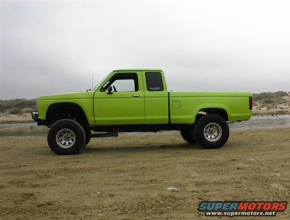 1986 Ford Ranger pickup truck, lifted, lime green paint, side view, parked on sand near water