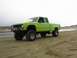 1986 Ford Ranger - This lifted pickup truck is parked on a sandy beach with a body of water and hills in the background.