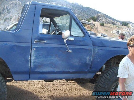 Blue SUV with dented door, parked on sand with rocky hills in background