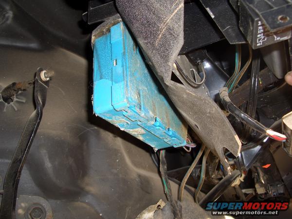 Close-up of a blue electronic control module and wiring harness inside a vehicle