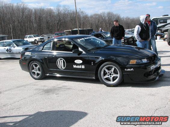 Black Ford Mustang Cobra with racing decals, parked at a track event. Another car with number 40 is visible