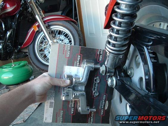 Hand holding a Kuryakyn USA part in packaging, with a motorcycle in the background