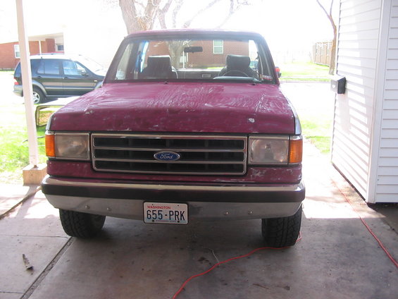 Maroon Ford Bronco with a dented front bumper and peeling paint, parked in a driveway