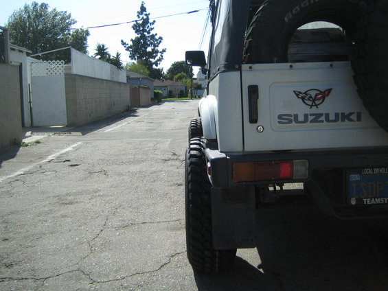 Rear view of white 1987 Suzuki Samurai with wide tires and a spare on the back