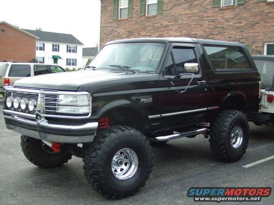 Black Ford Bronco with lifted suspension, chrome wheels, and off-road tires. Front grille and headlights visible