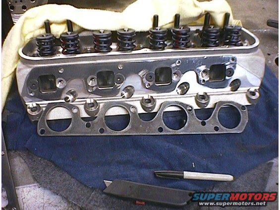Engine cylinder head with valve springs and exhaust manifold gasket, on a blue cloth with a utility knife and marker