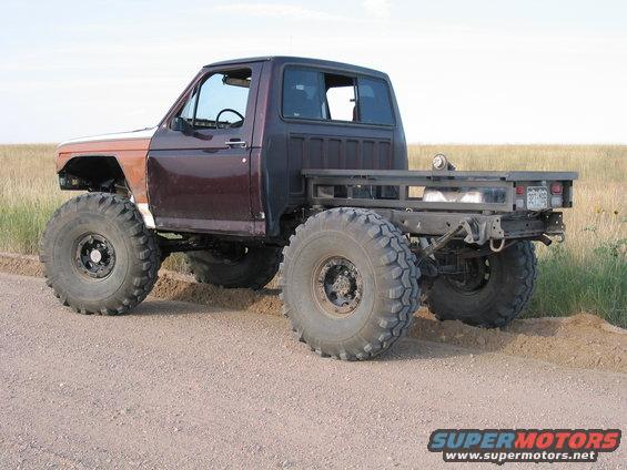 Custom truck with large tires, flatbed, and modified body panels. It has a dark purple cab and a brown fender