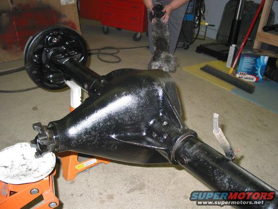 black rear axle assembly on jack stands, with a dog being held in the background
