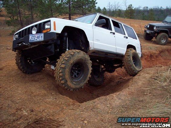 White Jeep Cherokee XJ with big tires climbing a dirt hill, another Jeep visible in background