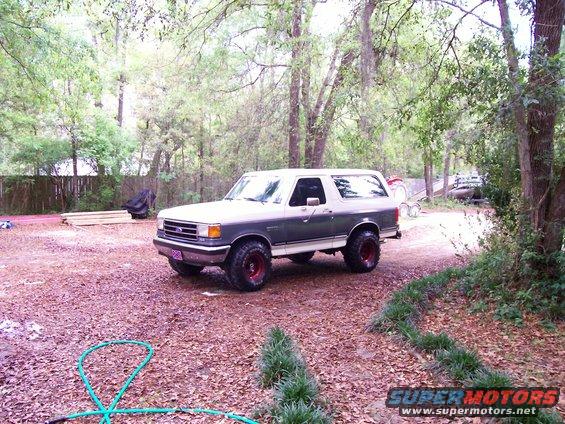 Two-tone gray and white Ford Bronco with red wheels parked on a gravel driveway