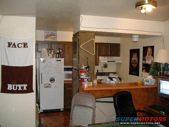 Interior view of a room with a refrigerator, kitchen counter, stove, and a computer monitor