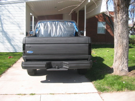 Rear view of a dark gray pickup truck with plastic-covered rear window