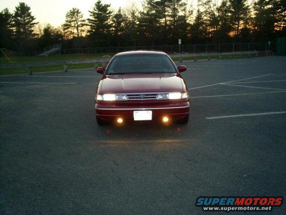 Red 1995 Ford Crown Victoria parked in a lot, front view, with headlights and fog lights on