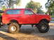 1987 Ford Bronco - This red Ford Bronco has been lifted with large off-road tires and has text written on the rear window.