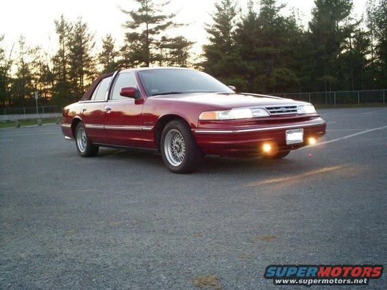 Red 1995 Ford Crown Victoria parked on asphalt, front quarter view, with trees in the background