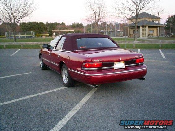 1995 Ford Crown Victoria sedan, rear view, parked in a lot with a building and trees in background