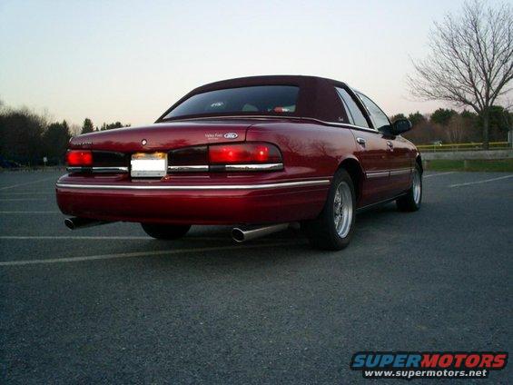 Red 1995 Ford Crown Victoria convertible sedan with dual exhaust pipes and chrome trim, seen from the rear