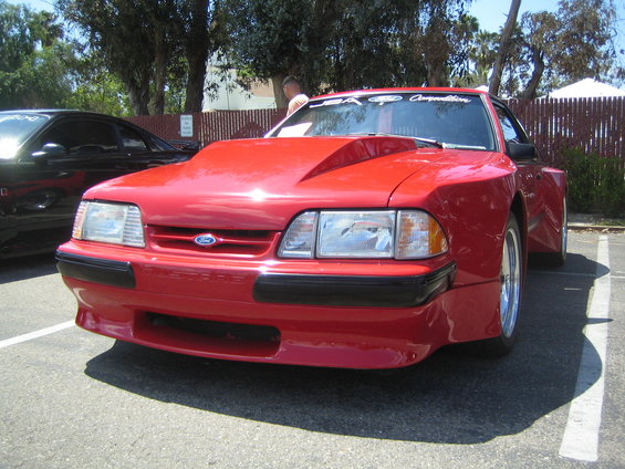 Red Ford Mustang with a large hood scoop and aftermarket wheels parked in a lot