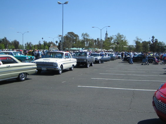 Line of classic cars parked in a lot, including a white 1963 Ford Falcon and a cream-colored car in the foreground
