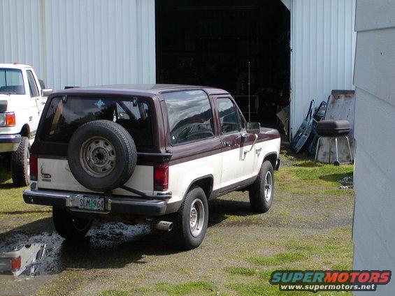 1987 Ford Bronco II parked in front of a garage with a white Ford truck to its left