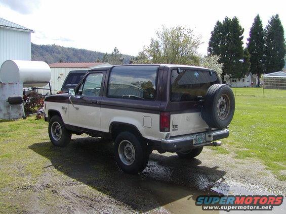 1987 Ford Bronco II, two-tone white and brown, with spare tire mounted on the rear door. Parked on a dirt lot
