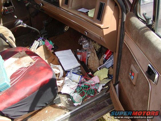 Interior of a cluttered vehicle, showing a red and black seat, dashboard, and door panel