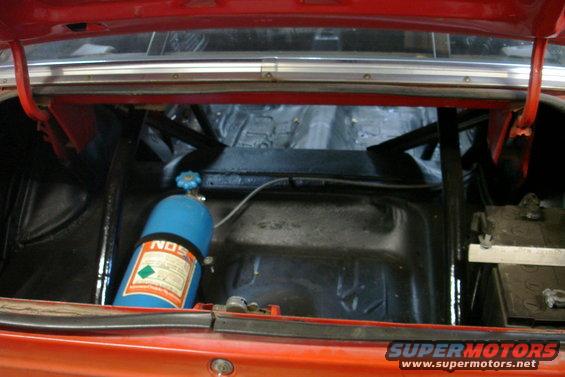 Red car trunk interior with a blue NOS tank, battery, and roll cage