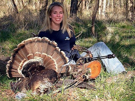 woman sitting in woods with a large turkey and bow