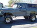 1979 Ford Bronco - Side view of a lifted Ford Bronco with off-road tires, showing body damage.