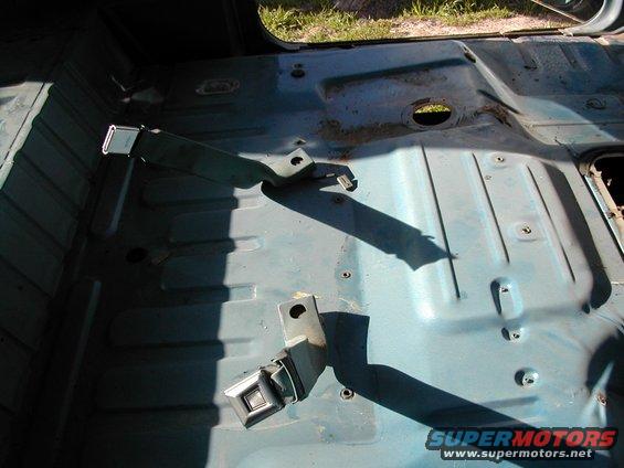 Interior floor of a vehicle with seatbelt anchors visible. Some rust spots on the metal