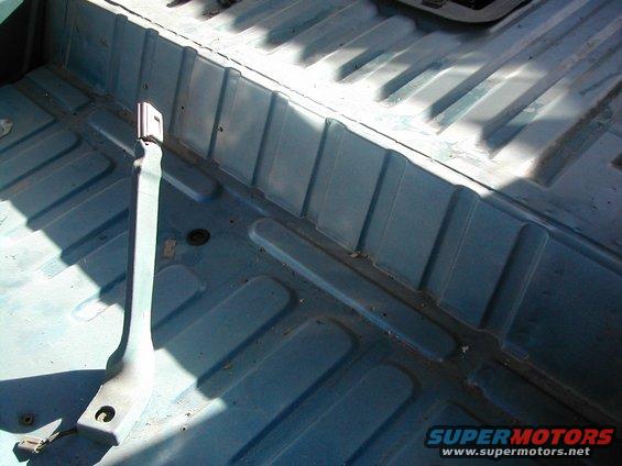 Interior floor of a vehicle with blue painted metal and seat belt anchor