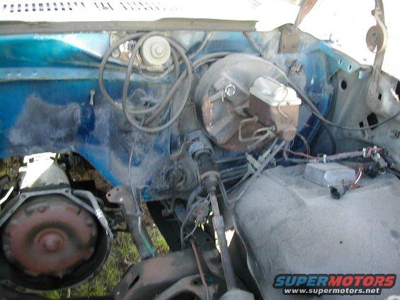 Close-up of a vehicle's engine bay, showing the brake booster, master cylinder, and transmission bell housing