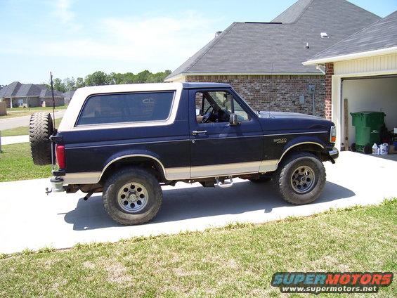 Dark blue 1992 Ford Bronco with a tan stripe and a spare tire mounted on the rear, parked on a driveway