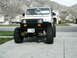 1995 Jeep Wrangler - White 1995 Jeep Wrangler with lifted suspension and large off-road tires parked on a driveway.