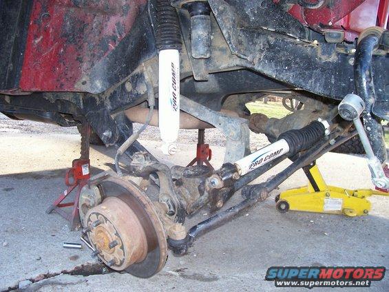Close-up of Jeep suspension and steering parts, including Pro Comp shocks, with vehicle on jack stands