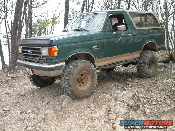 Green Ford Bronco with tan trim and large off-road tires on a rocky trail
