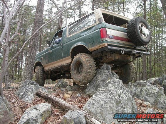 1990 Ford Bronco climbing over large rocks on a wooded trail