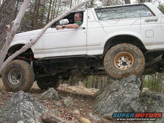 White 1992 Ford Bronco with lifted suspension driving over rocks