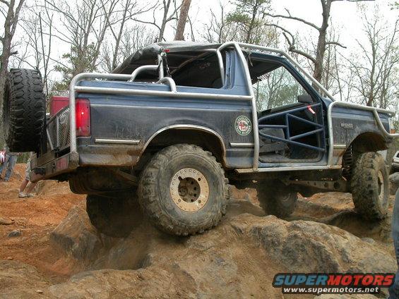 Blue off-road SUV with roll cage and spare tire on rear, climbing rocks