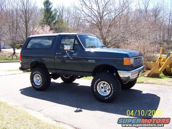 Dark blue 1987 Ford Bronco with lifted suspension and large tires, parked on asphalt