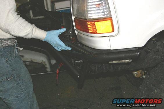 Person in blue glove working on aftermarket front bumper of a white SUV