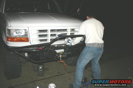 Front of a white 1995 Ford Bronco with a custom bumper and winch. Person is working on the grille