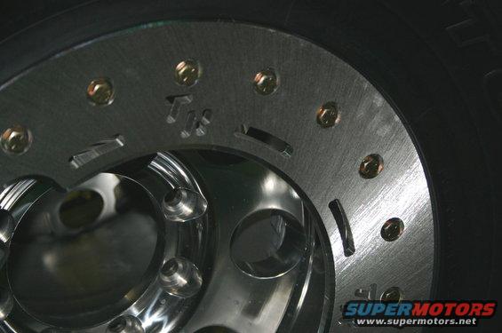 Close-up of a polished metal wheel with gold lug nuts and a black tire. Text 'Tx' is visible