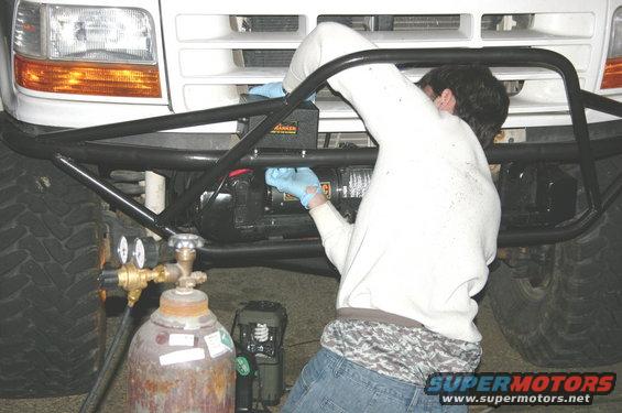 person working on winch mounted to front of truck, large tires visible