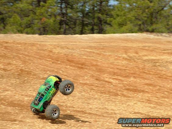 Green remote control monster truck doing a wheelie on a dirt track