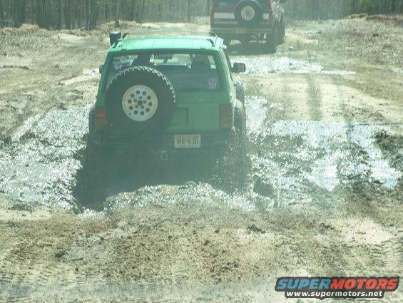 Green 1994 Ford Bronco driving through mud, another SUV behind it