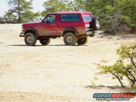 Red 1994 Ford Bronco on dirt road, spare tire on back