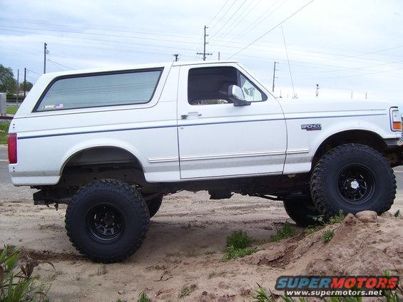 White 1994 Ford Bronco with lifted suspension and large tires, side view